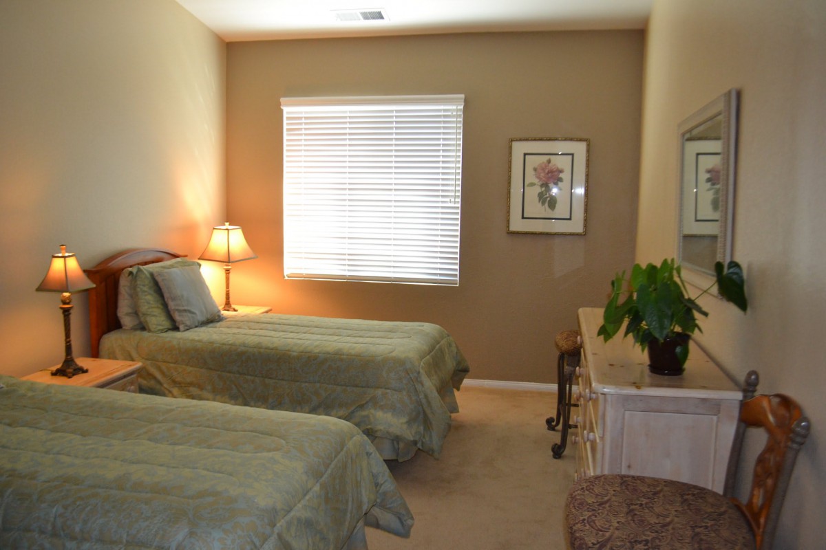 A cozy bedroom with twin beds, a lamp, and a dresser adorned with a plant.