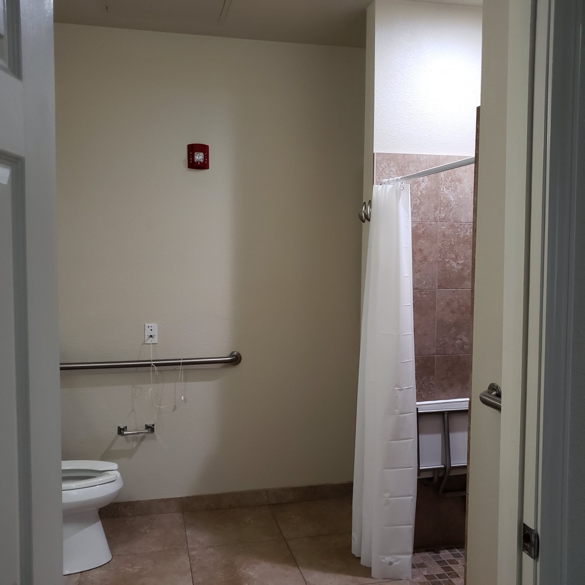 An accessible bathroom with a toilet, grab bar, and shower.