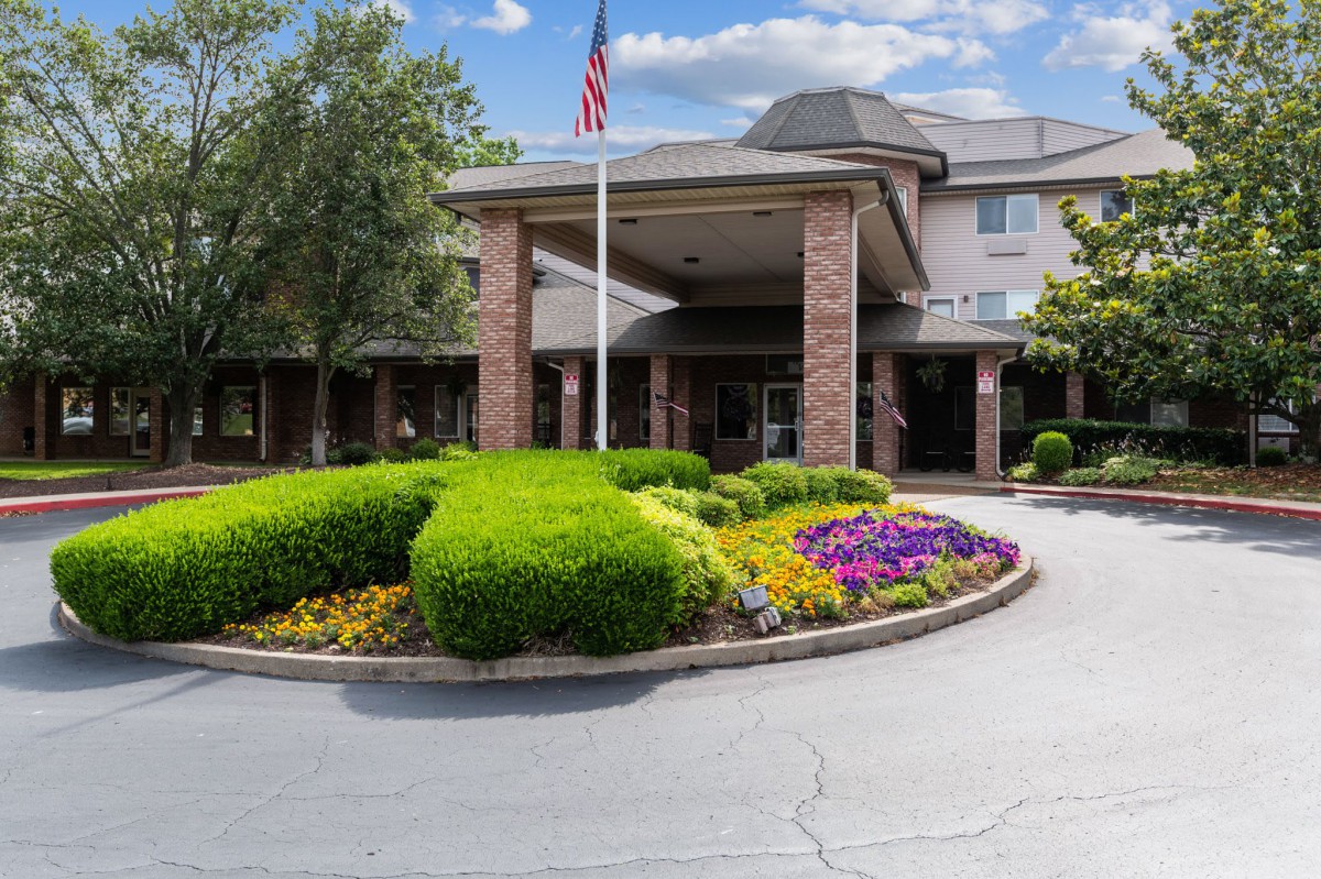 A well-maintained building entrance with landscaped gardens and an American flag flying overhead.