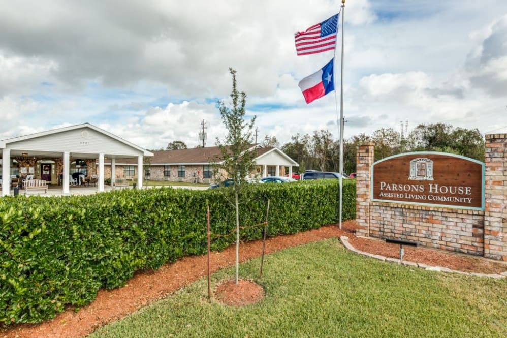 A nursing home entrance with American and Texas flags, surrounded by well-maintained landscaping.
