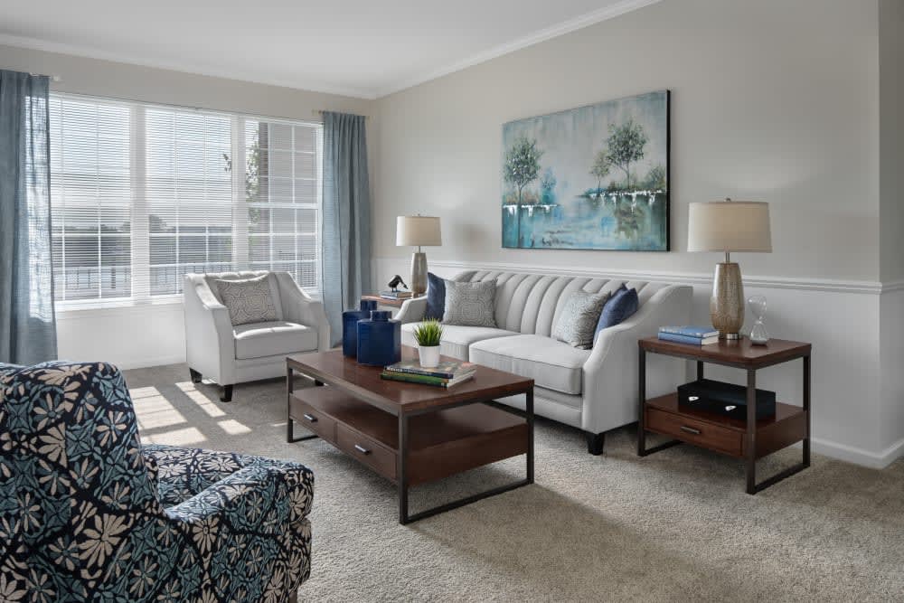 A cozy and well-lit living room with modern furnishings, including a sofa, armchair, coffee table, and decorative artwork.