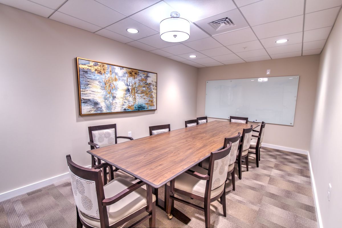 A modern conference room with a wooden table, surrounded by chairs and decorated with artwork on the wall.