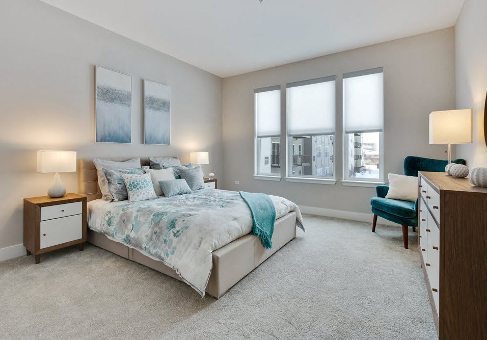 A modern and spacious bedroom with natural light streaming through large windows, featuring elegant decor and comfortable furnishings.