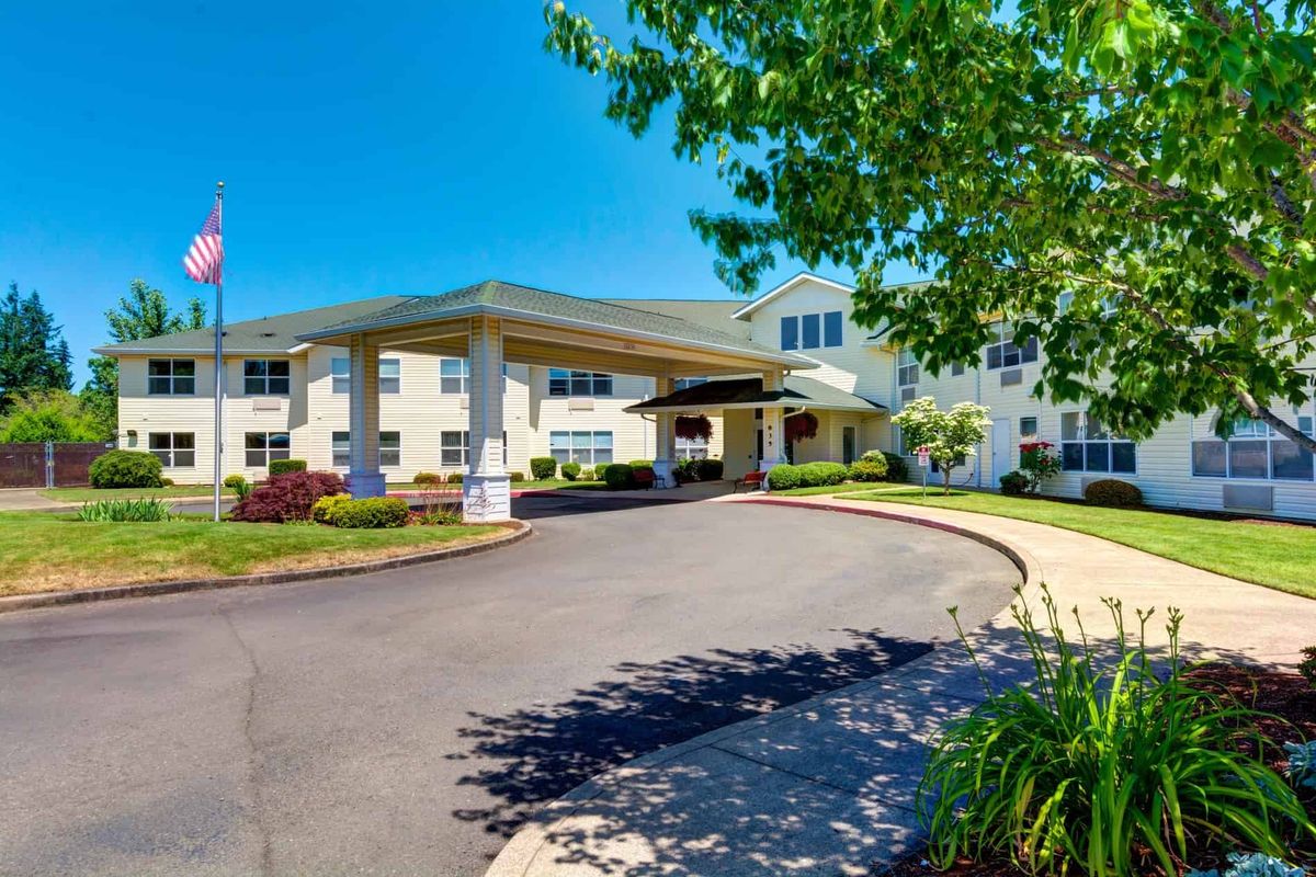 A sunny view of a residential building's entrance with a driveway and landscaped surroundings.