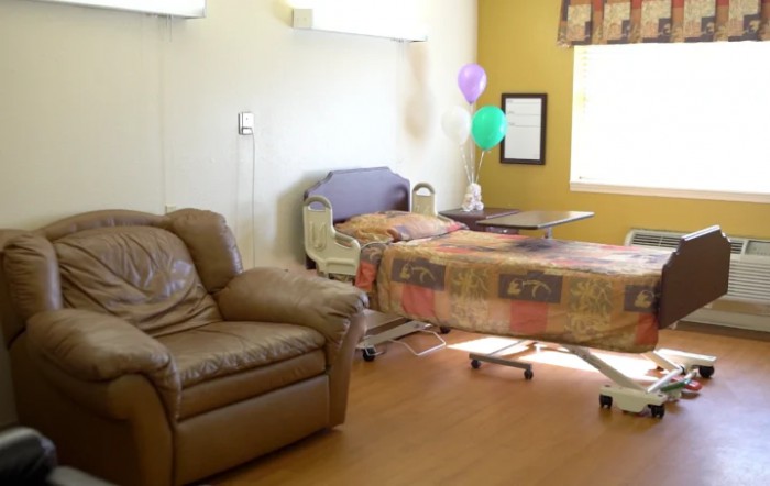 A hospital room with a bed, balloons, and a chair near a window.