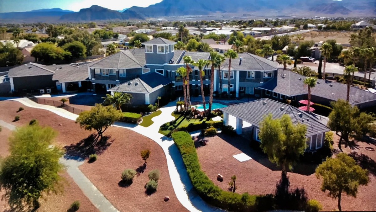 Aerial view of a large suburban house with palm trees and well-maintained landscaping.