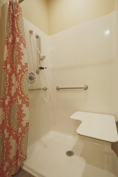 An accessible shower with grab bars and a foldable shower seat, featuring a patterned curtain.
