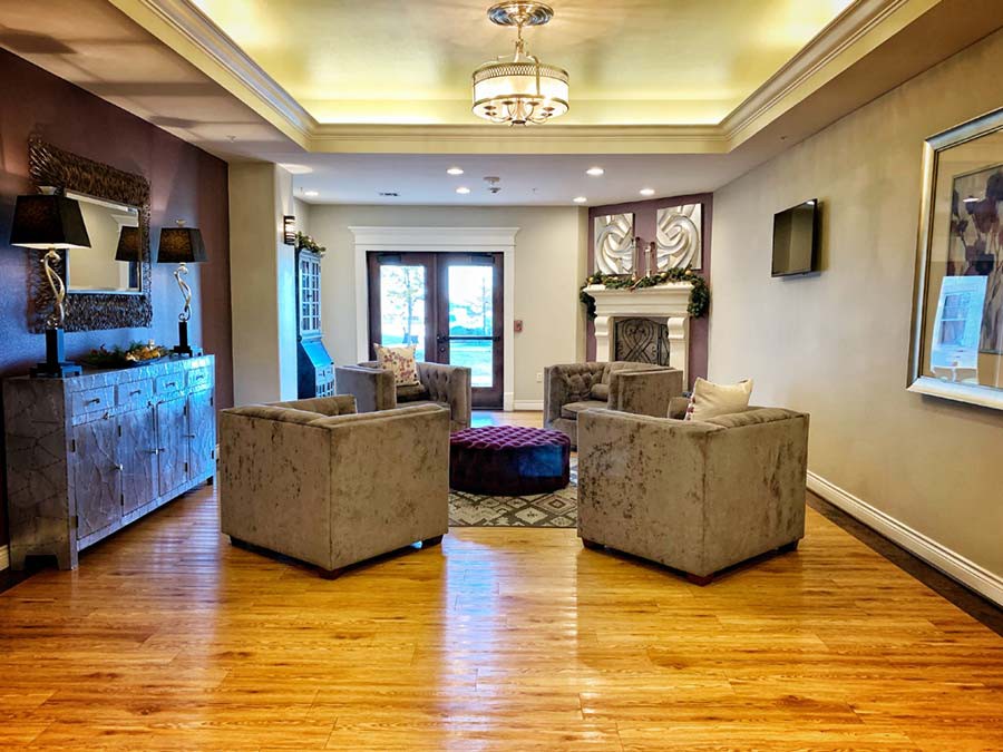 A cozy living room with plush chairs arranged around a central table, featuring a fireplace and elegant ceiling lights.