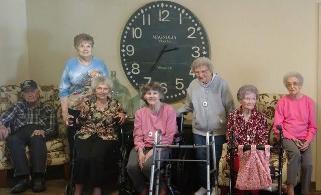 A group of elderly women posing for a photo in front of a large wall clock.