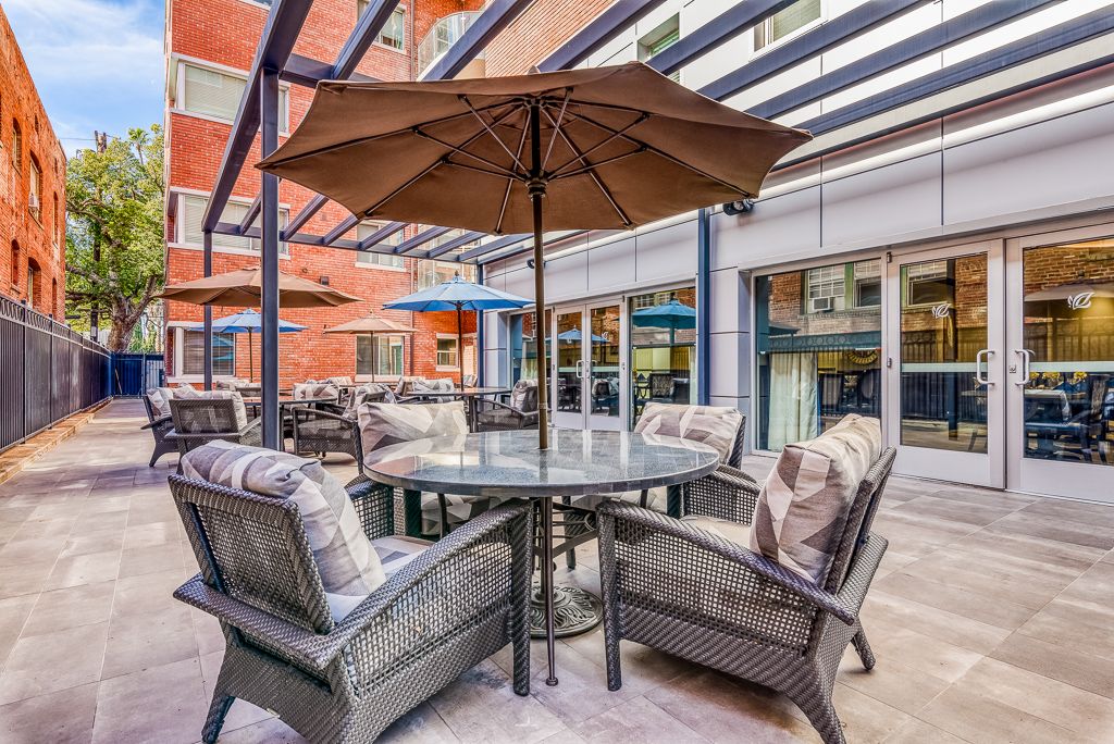 A cozy outdoor patio area featuring cushioned chairs surrounding a glass table under a large umbrella.