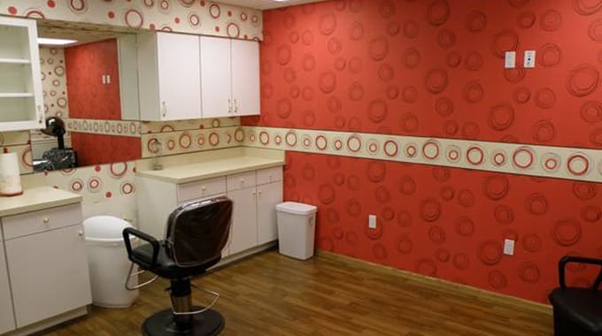 A salon room with red patterned wallpaper, a styling chair, cabinets, and wood flooring.