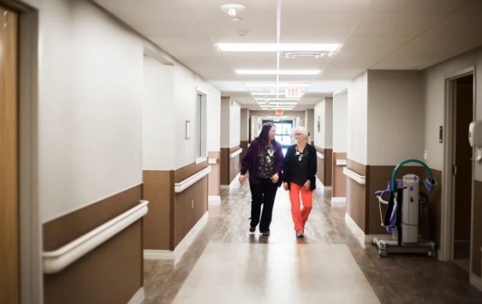 Two people walk down a hospital corridor.