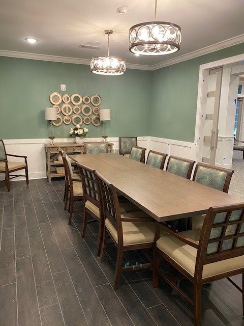 A well-furnished dining room with a large table, surrounded by chairs, and adorned with elegant chandeliers.