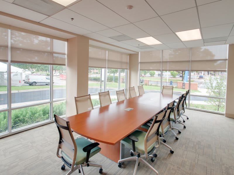 A bright and spacious conference room with a long table and office chairs, surrounded by large windows allowing natural light to fill the space.
