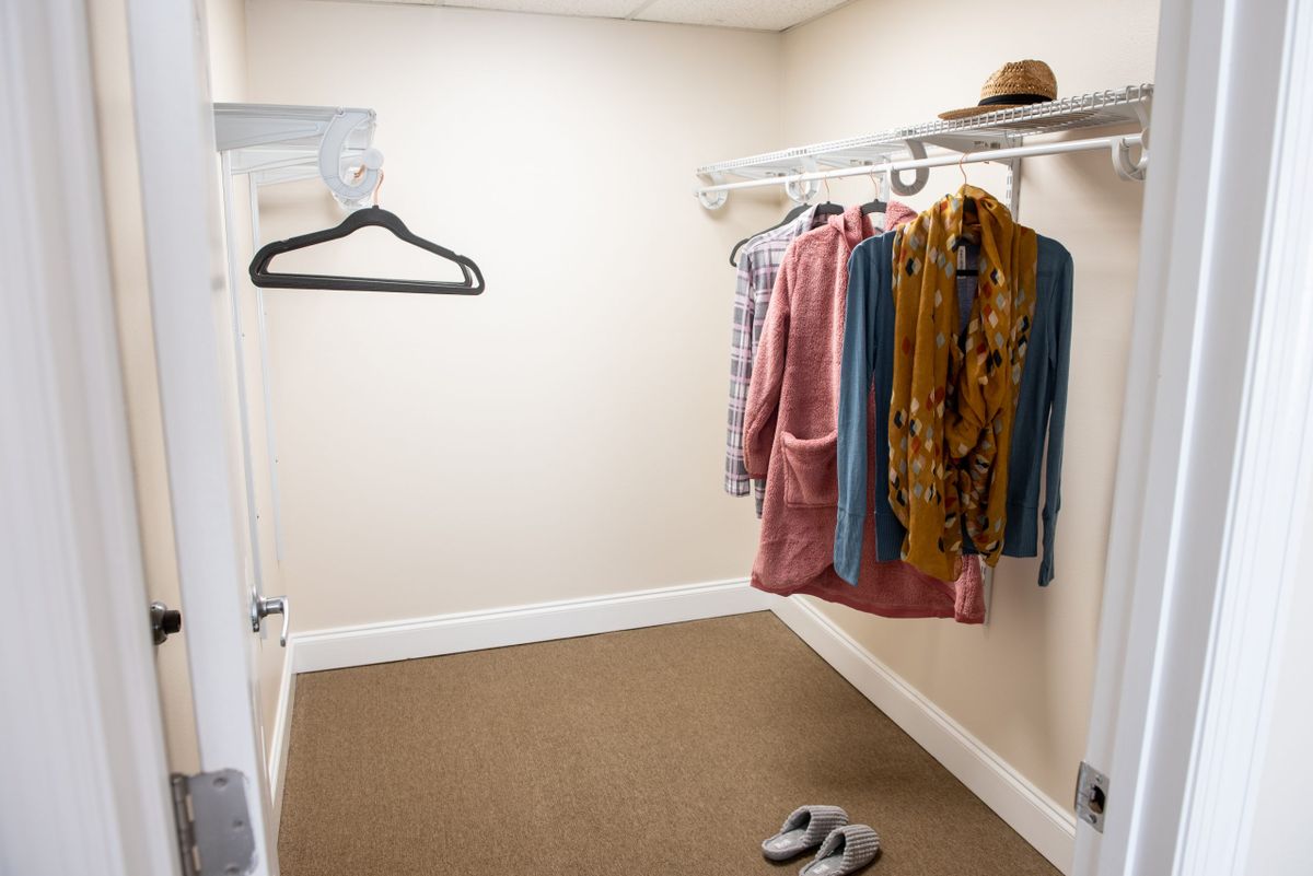 A tidy closet with hanging clothes, a hat, and slippers on the floor.