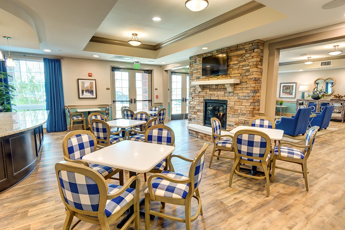 A cozy dining area with blue checkered chairs, tables, and a stone fireplace.