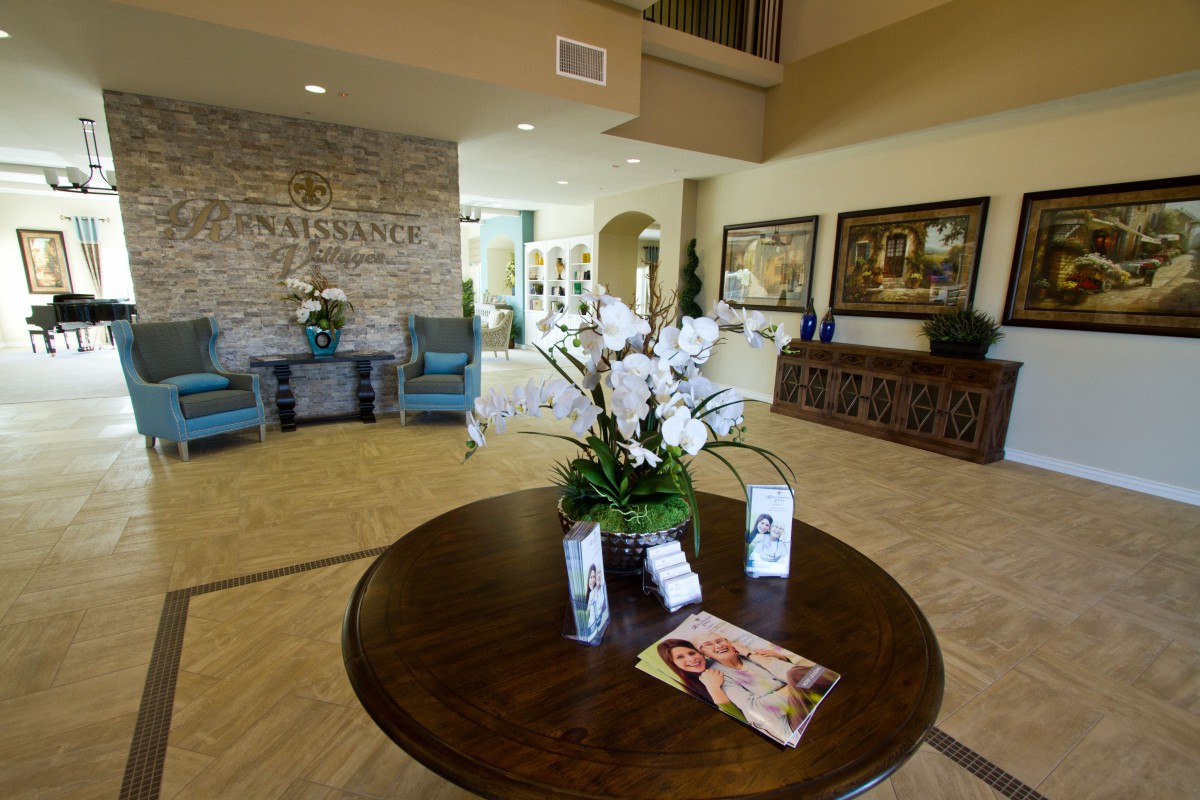 A well-decorated lobby featuring a central table with a floral arrangement and brochures, surrounded by comfortable seating and artwork on the walls.