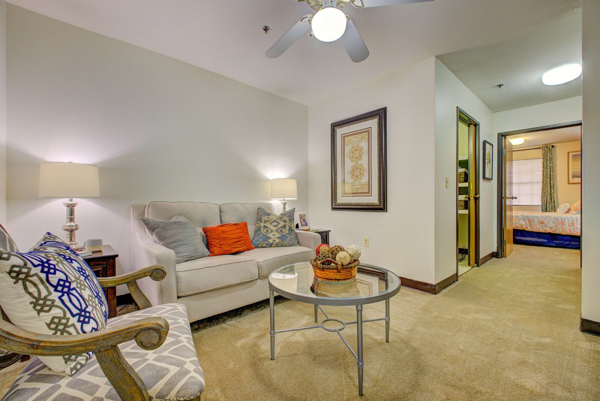 A cozy living room with a beige sofa, colorful cushions, and a glass coffee table, complemented by wall art and ambient lighting.