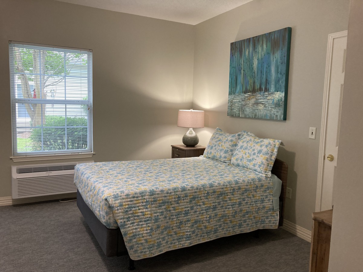 A cozy bedroom with a neatly made bed, lamp on the nightstand, and artwork on the wall.