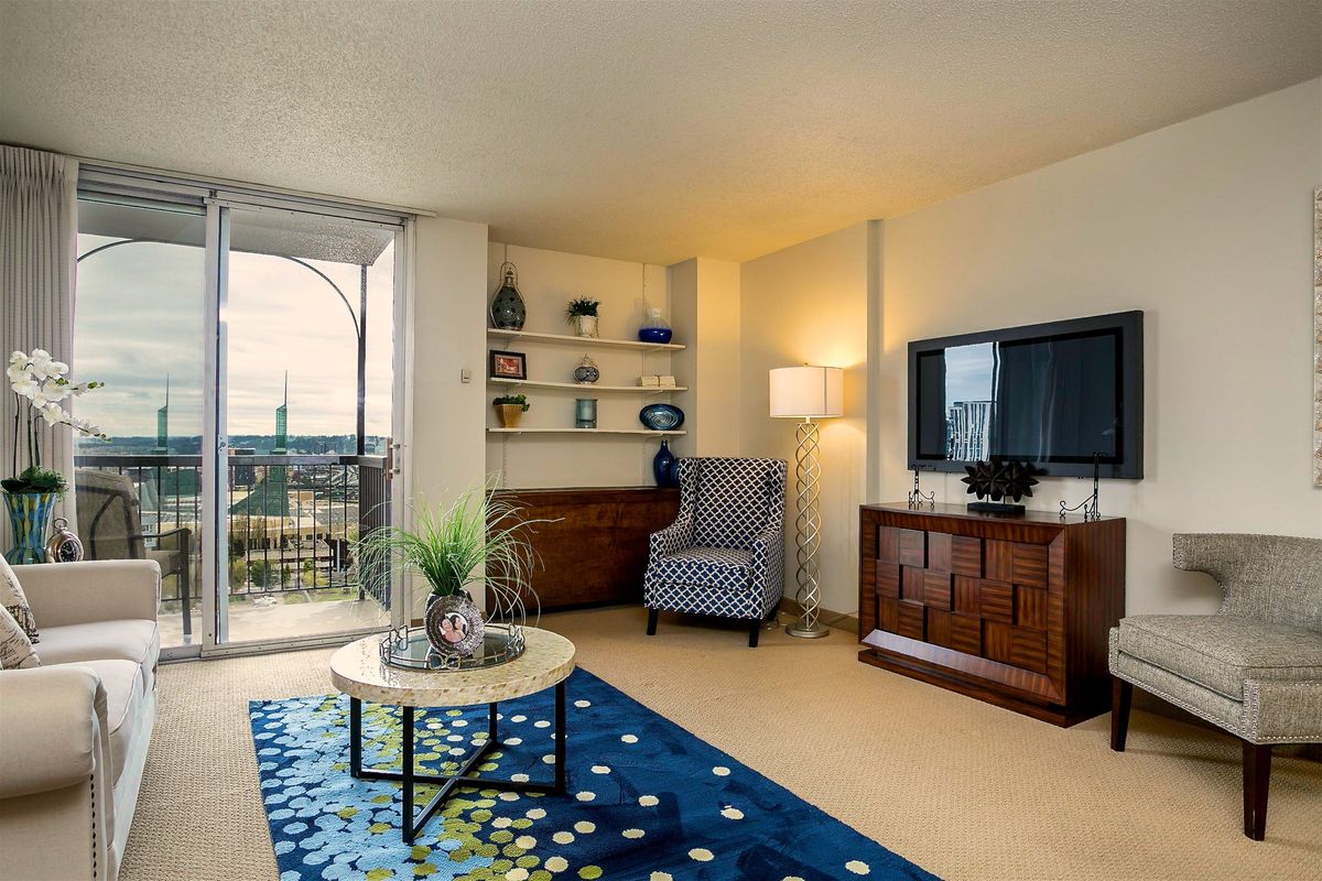 A cozy living room with modern decor, featuring a bookshelf, television, armchair, and balcony overlooking the outdoors.
