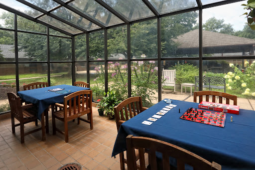 A serene sunroom featuring wooden tables and chairs, with a lush garden view through glass walls.