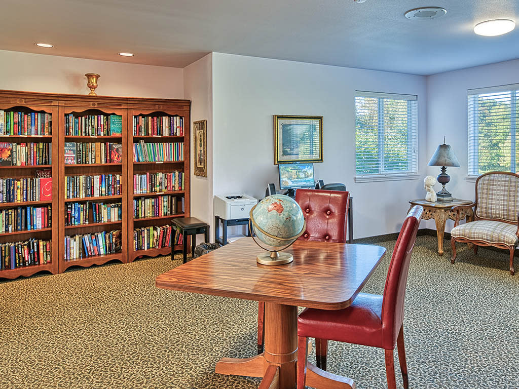 A cozy library room with bookshelves, a table with a globe, and two leather chairs.