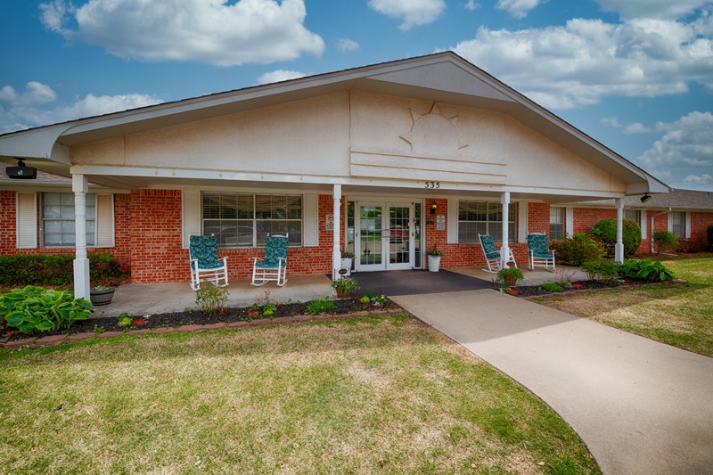 A welcoming entrance to a brick building with a porch and well-kept landscaping.