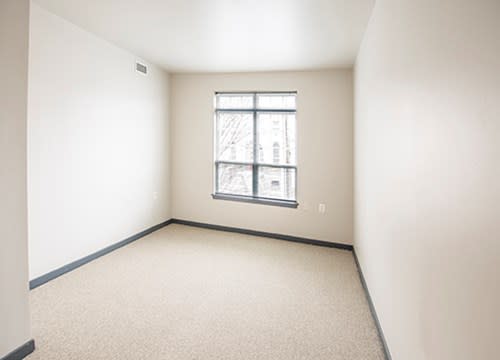 An empty room with beige walls, a carpeted floor, and a window letting in natural light.