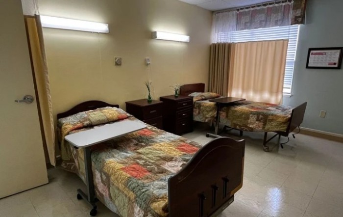 A hospital room with two beds equipped with overbed tables and curtains.