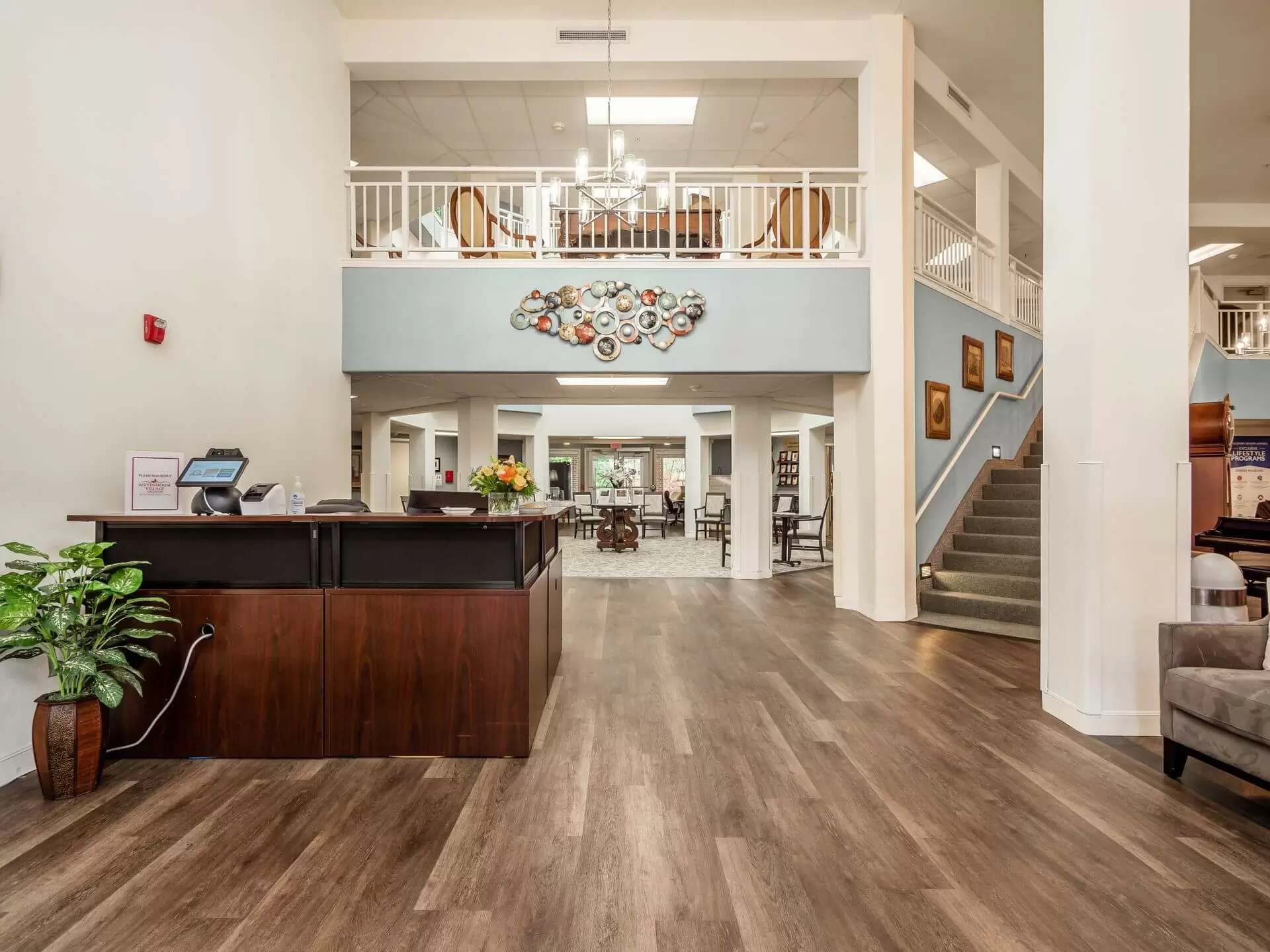 A spacious modern lobby with a wooden floor, featuring a reception desk and staircase.