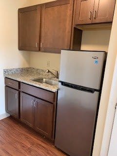 A compact kitchen with wooden cabinets, a sink, and a stainless steel refrigerator.