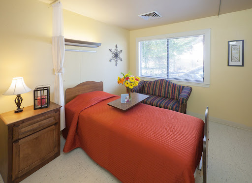 A cozy and well-lit bedroom featuring an orange bedspread, a comfortable sofa, and vibrant flowers.