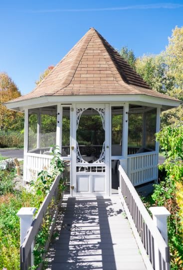A charming wooden gazebo set amidst a lush garden with a pathway leading to its entrance.