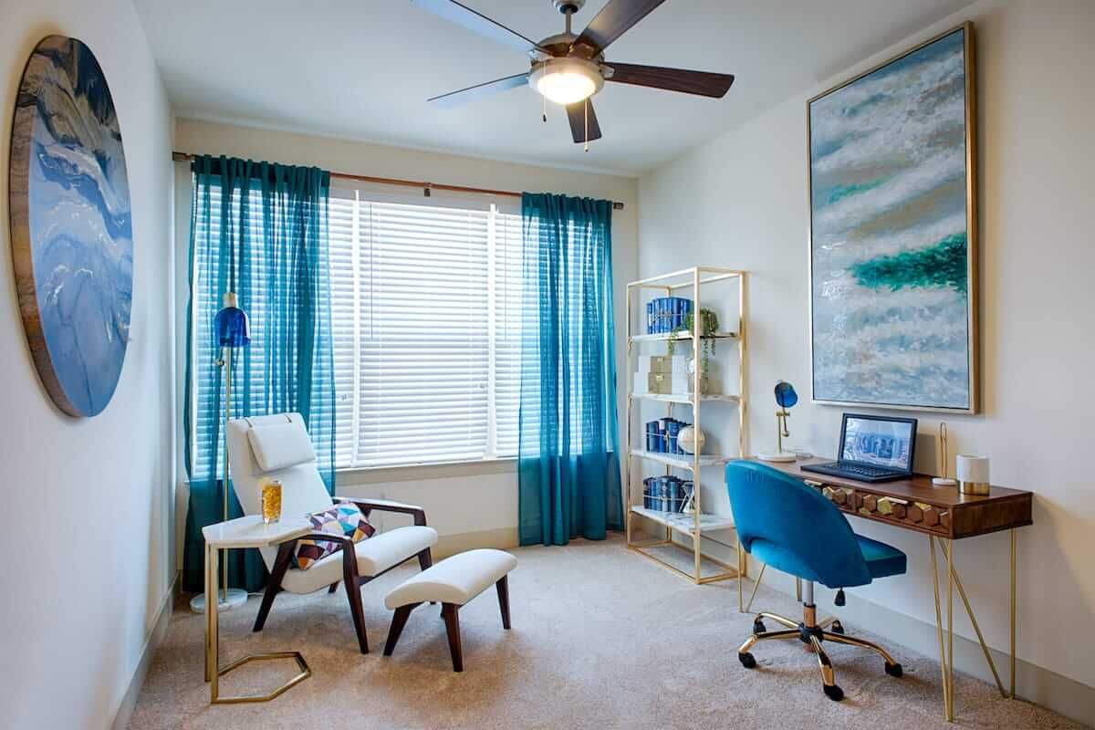 A modern home office with blue accents, featuring a desk, chair, and bookshelf.