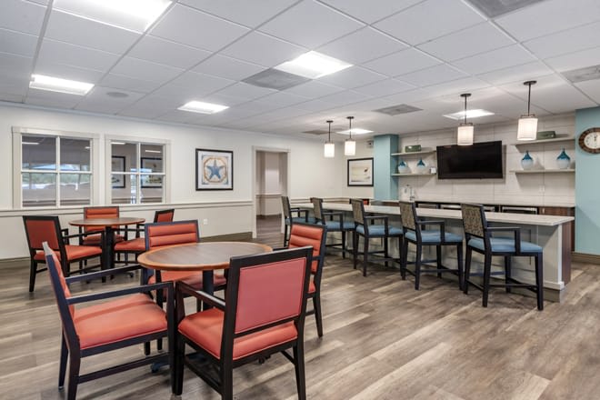 A modern dining area featuring tables and chairs with a bar counter in the background.