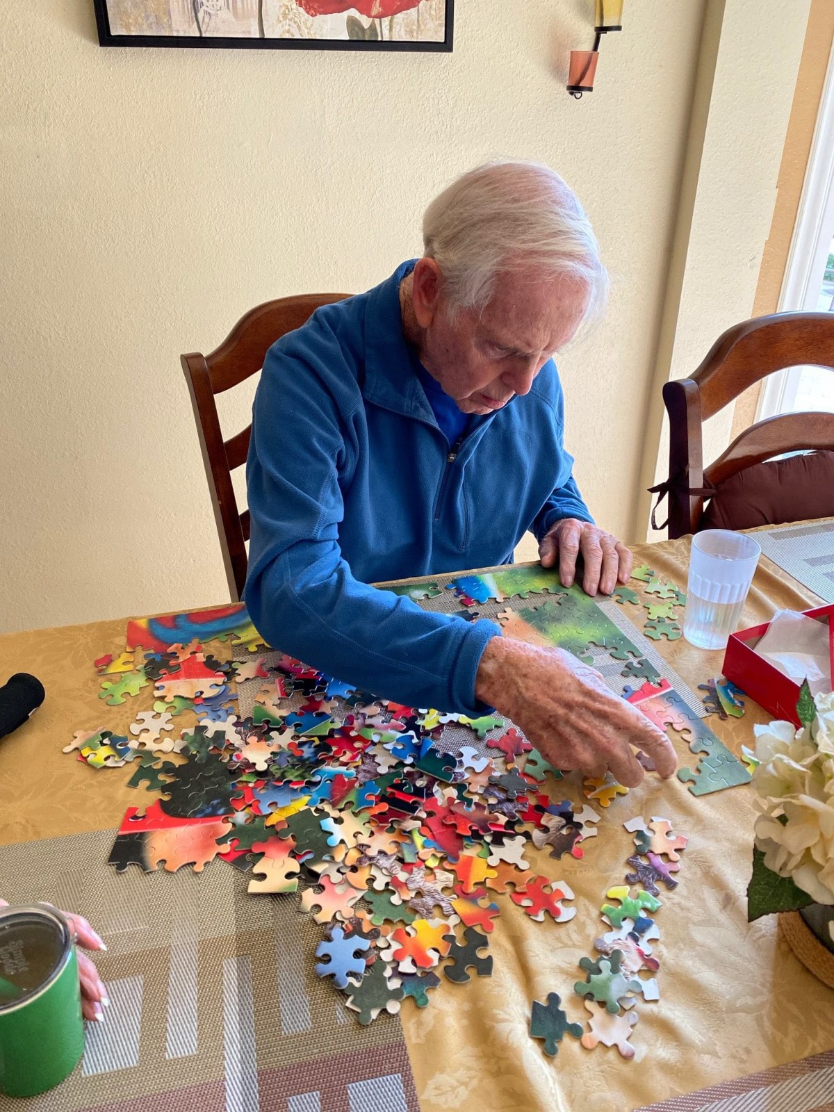 An elderly person working on a colorful puzzle at a table indoors.