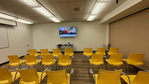 A modern waiting room featuring yellow chairs and a TV screen.