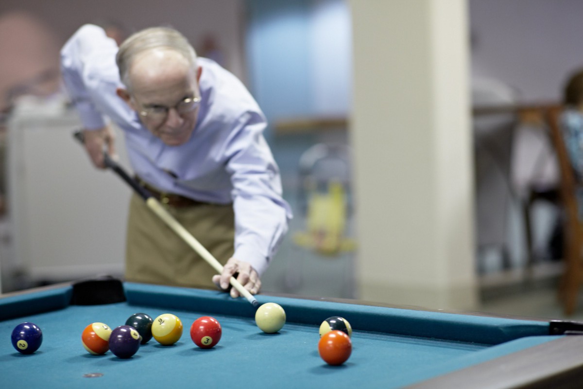 An elderly man playing pool, focused on making a shot.