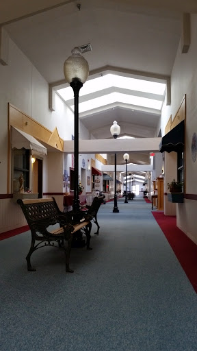 A quiet indoor shopping mall corridor featuring benches and decorative lampposts.