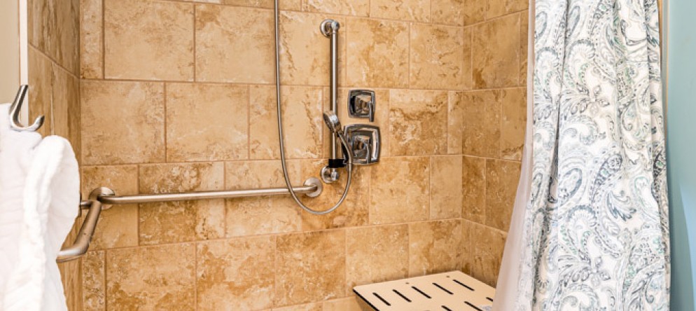 Accessible shower with grab bars and a bench in a tiled bathroom.