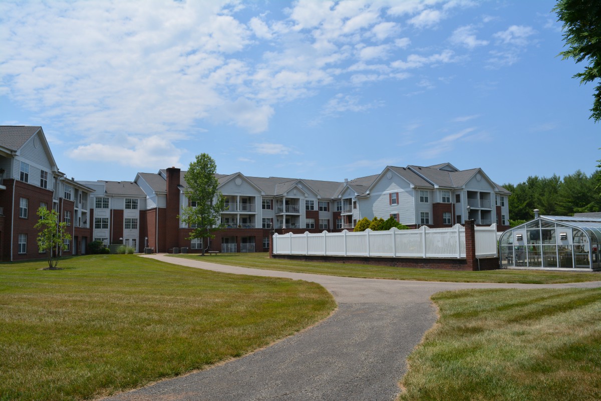 A modern apartment complex with a pathway and landscaped surroundings under a cloudy sky.