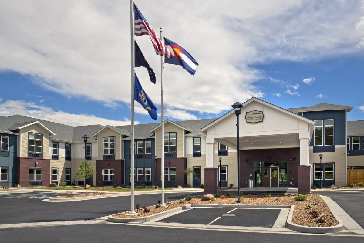 A modern building with flags flying outside above a parking lot under a cloudy sky.