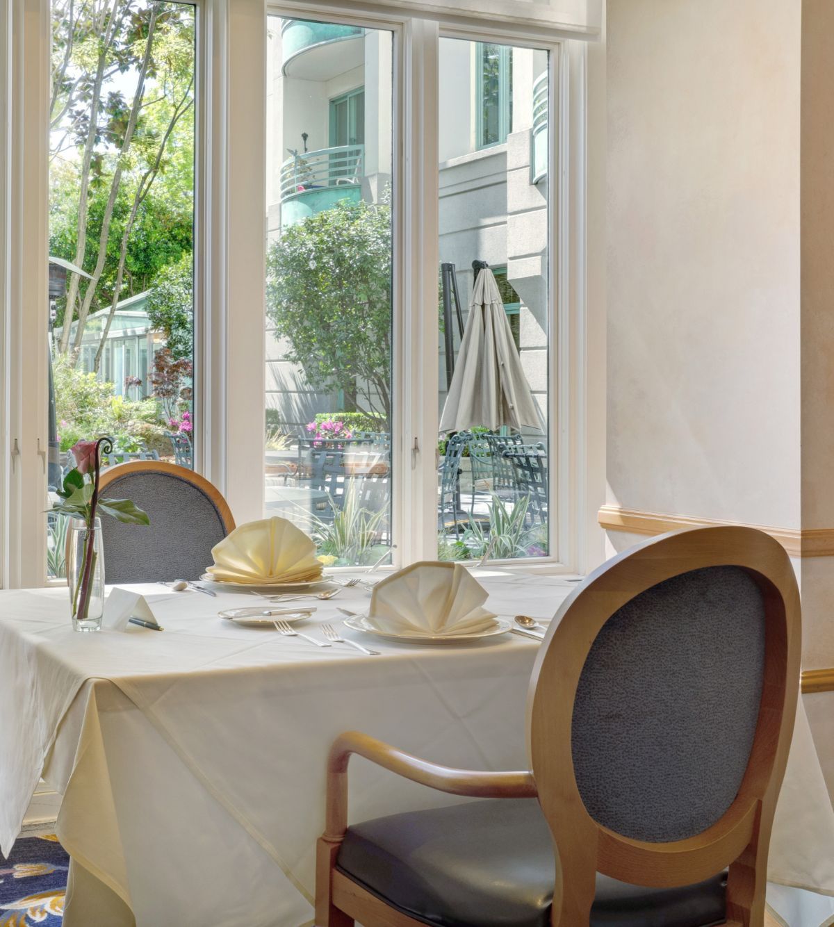 A beautifully set dining table by large windows with a view of the garden.