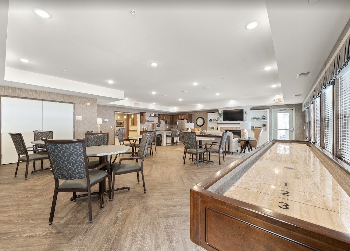 A spacious community room with various seating areas and a shuffleboard table.