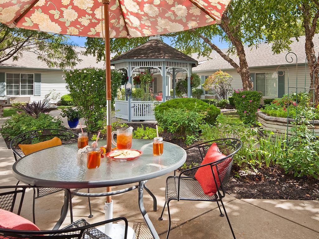 A cozy patio setup with a table, umbrella, and chairs overlooking a lush garden and gazebo.