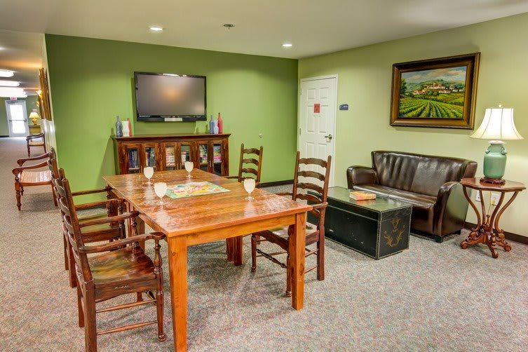 A cozy conference room with a wooden table, chairs, and a television on a green wall.