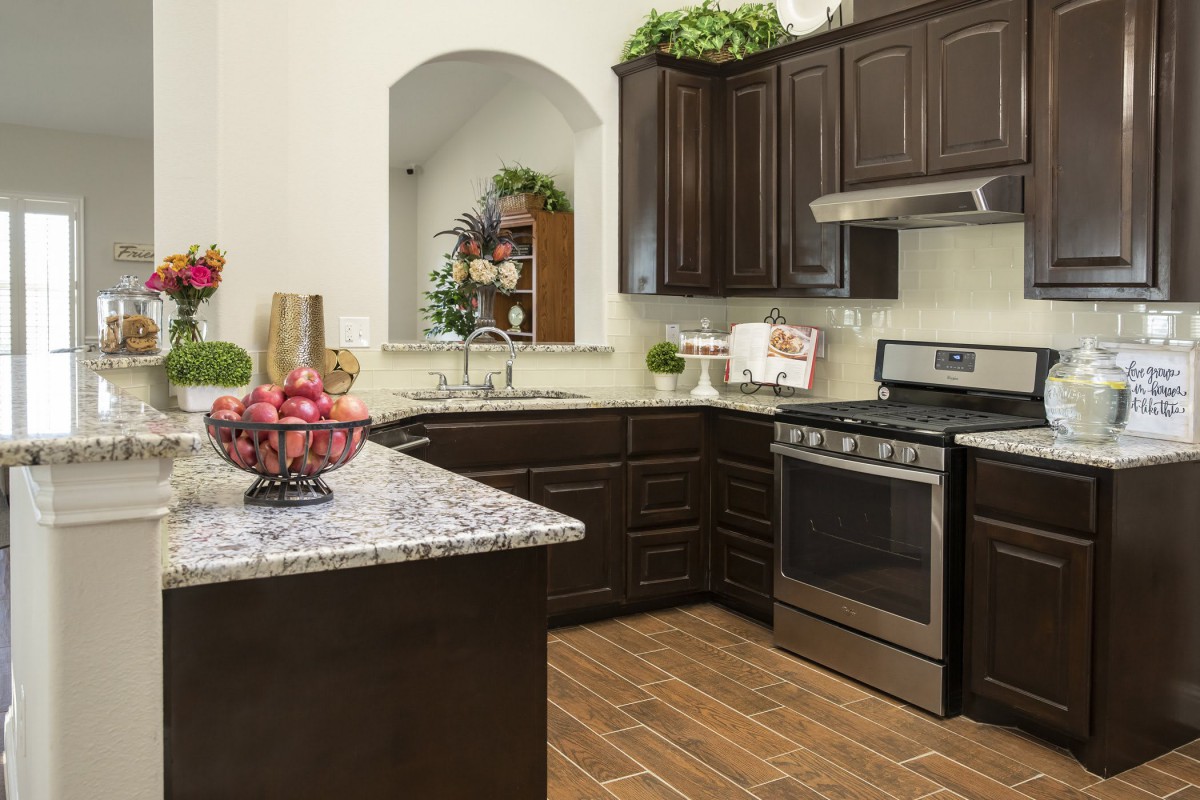 A modern kitchen featuring dark cabinets, stainless steel appliances, and a granite countertop adorned with decorative plants and a fruit bowl.