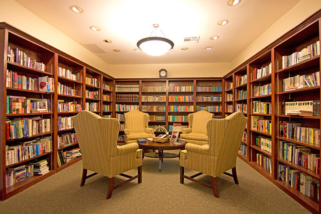 A cozy library with armchairs surrounded by bookshelves filled with books.