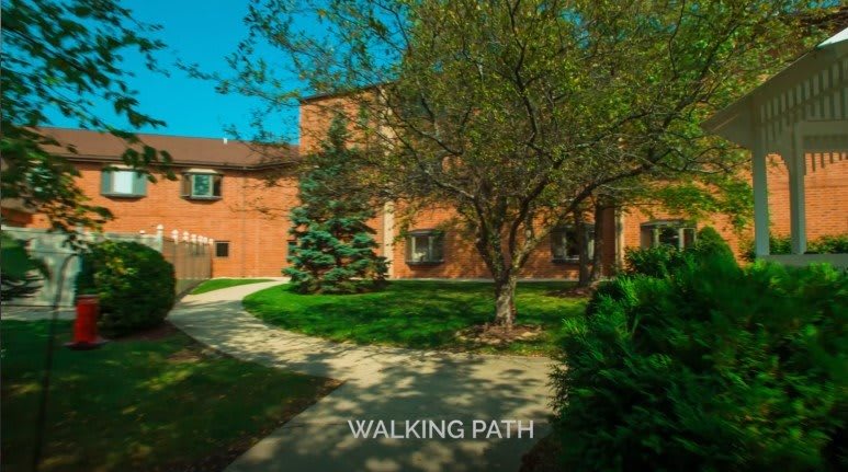 A brick residential building with a tree-lined walking path in front.