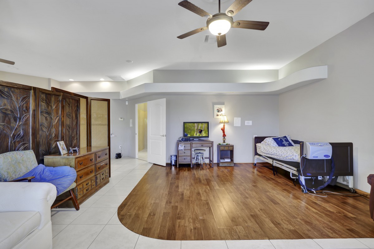 Spacious bedroom with wood flooring, featuring a ceiling fan, dresser, television, and a desk.